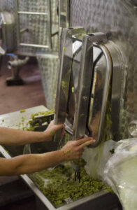 man open tank's door and collected grape skins into a vat at Vegoritis Winery plant