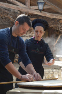 In the heartwarming picture, a woman wearing a black cooking uniform is joyfully assisting a man in preparing the dough for the pie. Their teamwork and shared passion for cooking shine brightly, creating a delightful culinary moment.