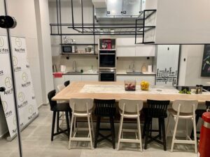Modern kitchen with a large wooden table, black and white chairs, and sleek appliances, including a stylish fridge that completes the contemporary aesthetic.