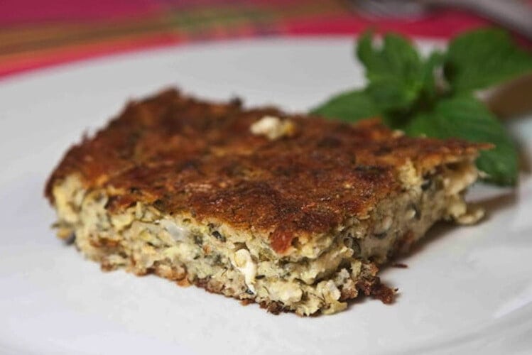 close-up of piece of &lsquo;Kolokythopita&rsquo; means zucchini pie with green herbs in the background 