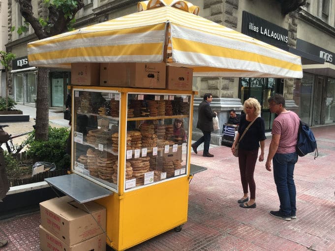 Kiosk with Greek &lsquo;Koulouri&rsquo;, round-shaped breads topped with sesame seeds on the street and a couple watching them 