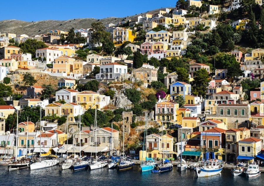 Symi food tours - Gastronomy Tours boats anchored in the port of Symi island in Greece and buildings on the mountain in the background