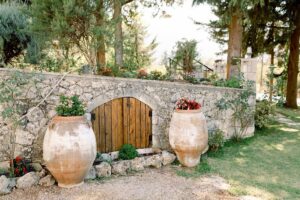 a double wood door of stone low building with two flower pots on the both sides at Dourakis Winery outside