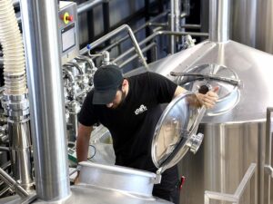 a worker opens the lid of the tank and looks inside at Pineios Brewery plant