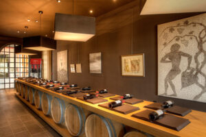table from wood barells with wine bottles in the background of paintings on the wall of 'Domaine Skouras'