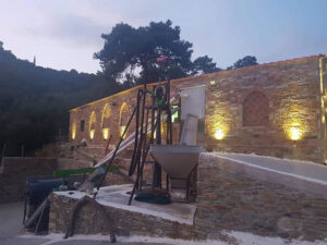 old press olive in front of the illuminate 'Eirini Plomariou' stone building