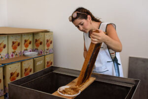girl collecting honey comb using a bee hive scraper knife from the honeycomb panel at 'Ermionis'