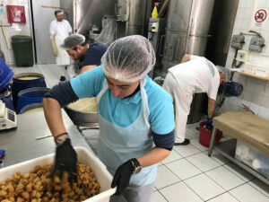 woman with gloves mixing composition in a bucket at 'M. Kosmidis' workshop with anothers workers in the background