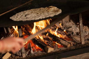 woman baking pitta bread into stone oven at Ktima Perek