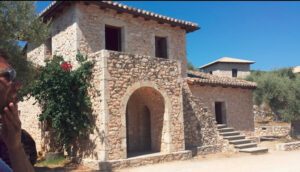 one side of the building with stone walls and flowers of 'Lefkaditiki Gi'