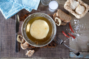 view from above of bowl with 'Mystakelli Dairy' white cheese in oil and pieces of dry bread and two garlics