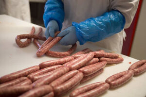 man with blue plastic gloves putting fresh sausages on white table at Vavourakis Farm workshop