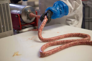 man with black plastic glove holding sausage and stuffing it through machine at Vavourakis Farm workshop