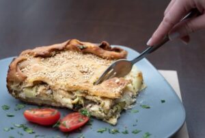 Boureki - Gastronomy Tours a hand holding a fork over a piece of food