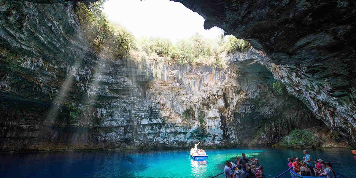 The Best Kefalonia food tours - Gastronomy Tours A small boat navigates the vibrant blue waters within a cave, highlighting the natural beauty of the surrounding rock walls.
